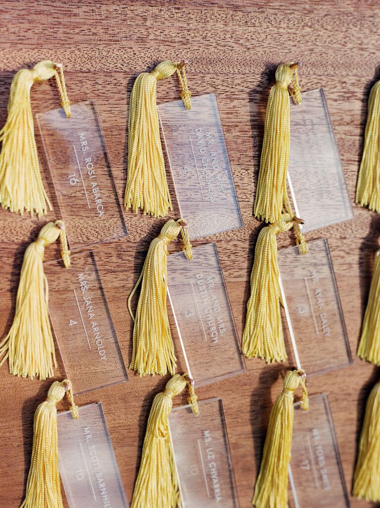 acrylic wedding escort cards hanging on wooden display board with yellow tassels 2022 wedding colors 