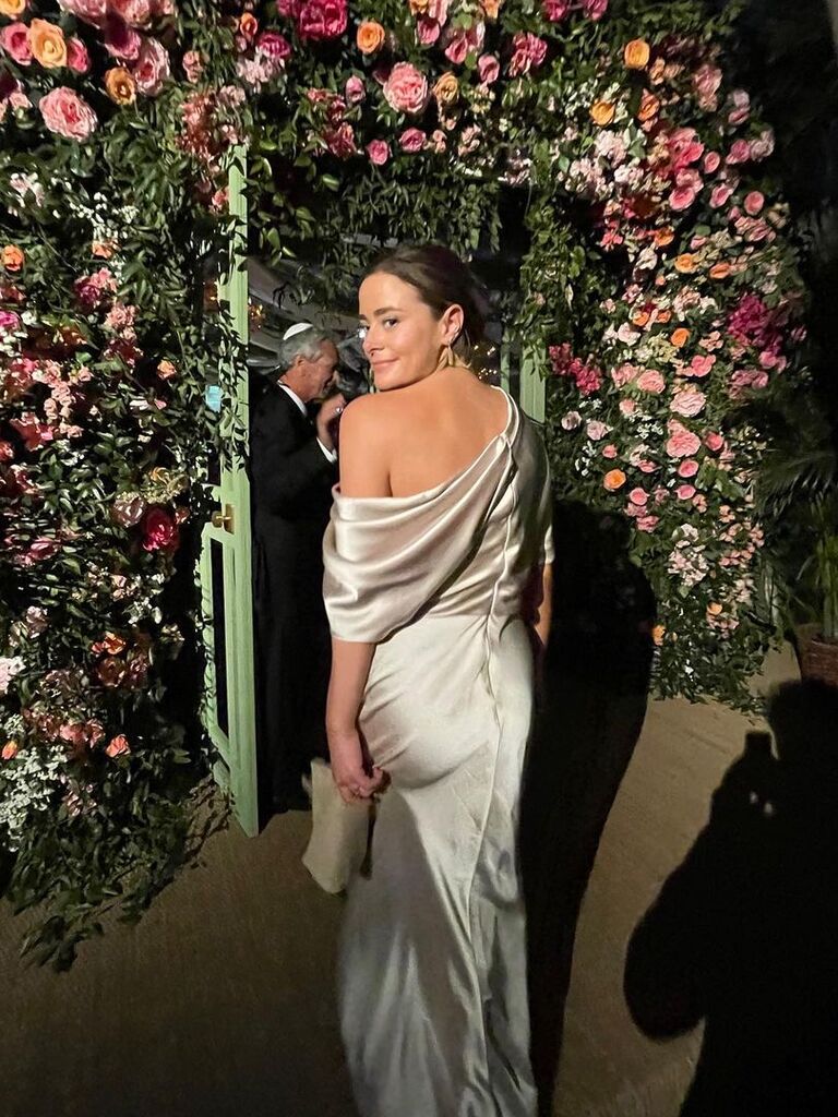 Naomi Biden smiles over her shoulder while walking under a flower arch. 