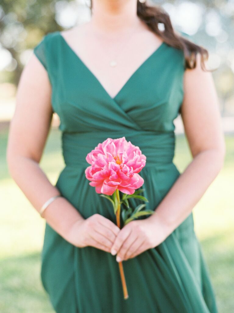 A bridesmaid holds a single vibrant pink flower.