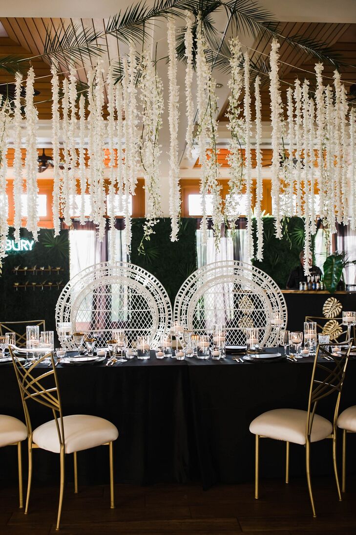 Modern Dining Table with Black Tablecloth, Wicker Sweetheart Chairs and Hanging Flowers