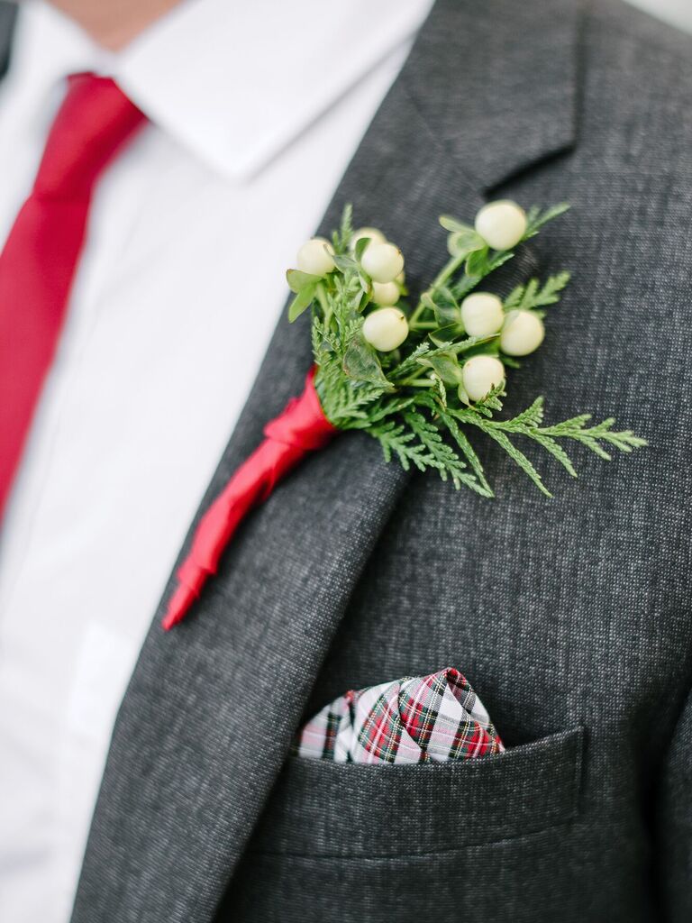 close up of winter wedding boutonniere with white berries, evergreens, red plaid pocket square and matching red tie