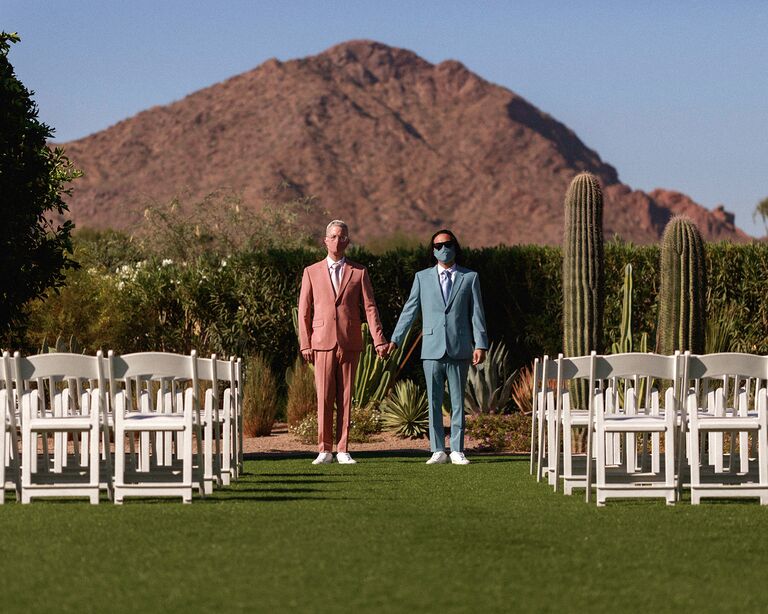 couple holding hands with masks on and suits