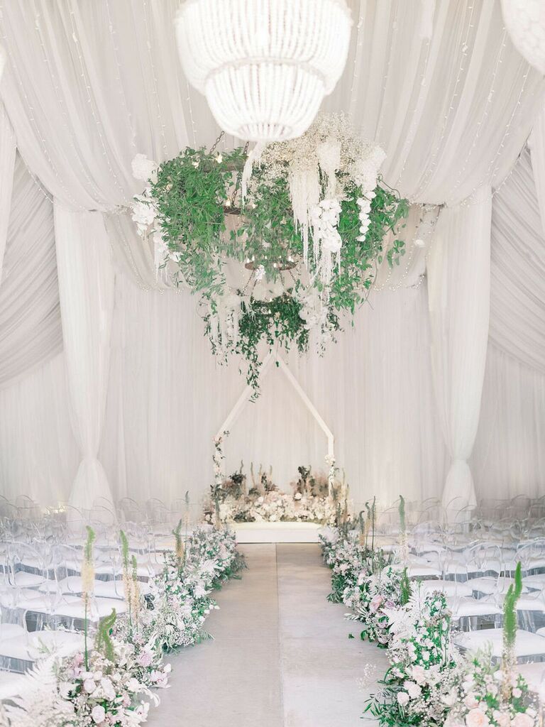 glam wedding ceremony with white and greenery flower chandelier with white drapery around the walls