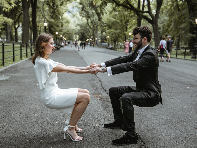 Couple holds hands and squats for a funny photograph in Central Park. 