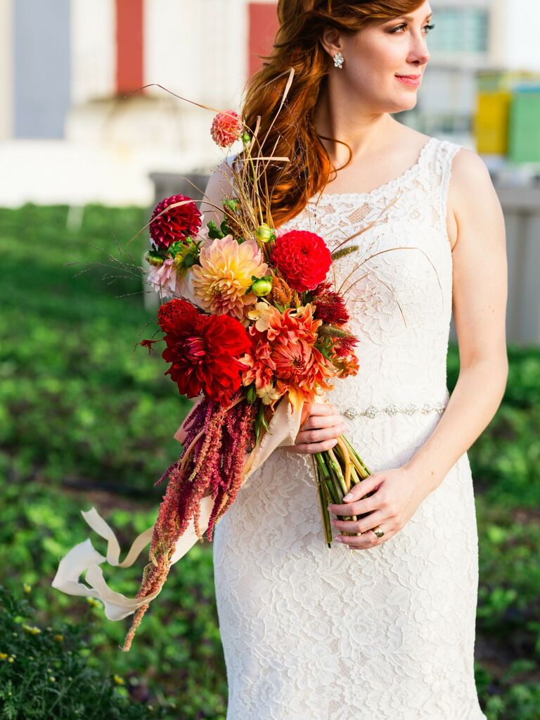 Bride holds a bouquet of vibrant red dahlias. 