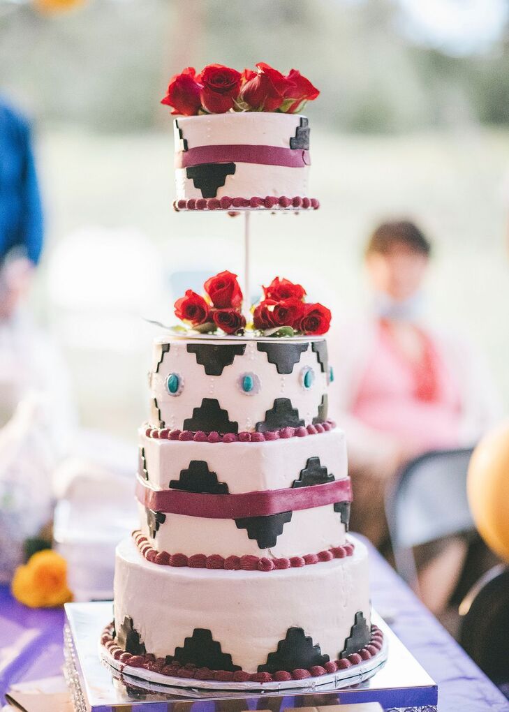 A four-tier, geometric white wedding cake with intricate fondant designs and rose accessories as a dessert for a traditional Native American Navajo wedding.