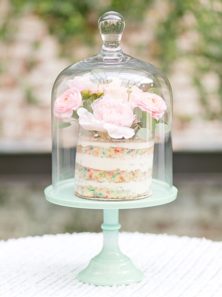 milk bar wedding cake displayed in glass cloche jar with fresh flowers on top