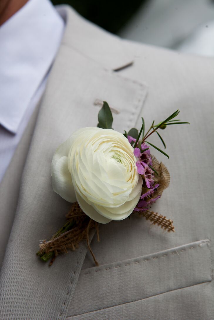 The groom's boutonniere was created by New Creations Florals using a white ranunculus, purple wax flowers and scabiosa pods with burlap wrapped around the base.