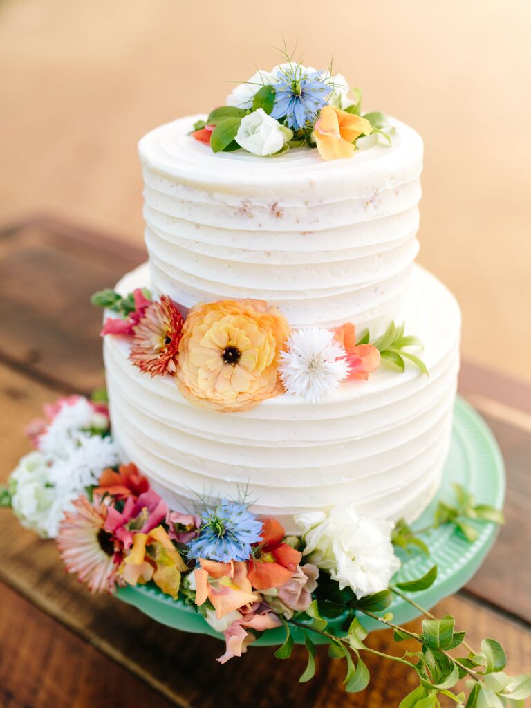 two tier buttercream wedding cake with blue yellow orange and pink wildflowers