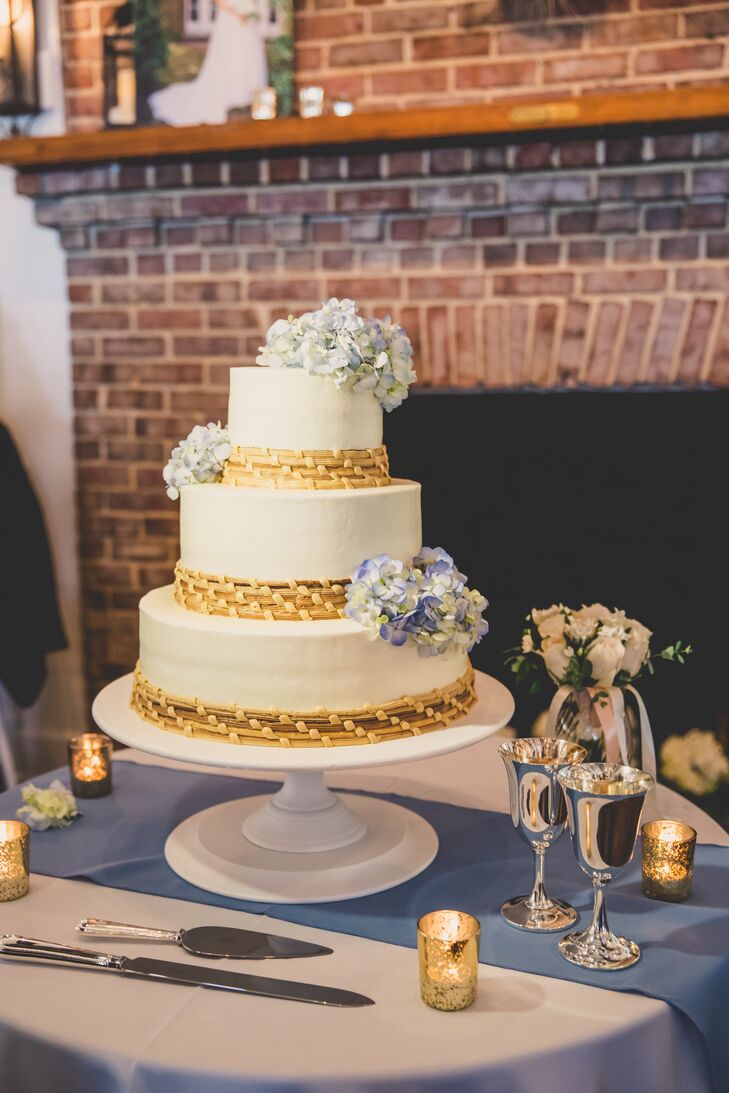 The white wedding cake for dessert was decorated with blue hydrangeas and accents of sweetgrass basket weaving, a craft native to the lowcountry regions. The cake was displayed on an antique white cake stand on a blue and white cake table.