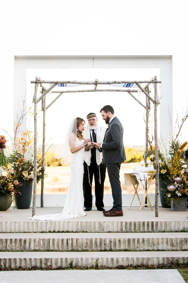 Couple exchanging rings under birch wood chuppah.