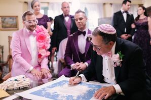 Jewish Grooms in Bold, Pink-and-Purple Tuxes Watch as Rabbi With Colorful Kippah Signs Ketubah