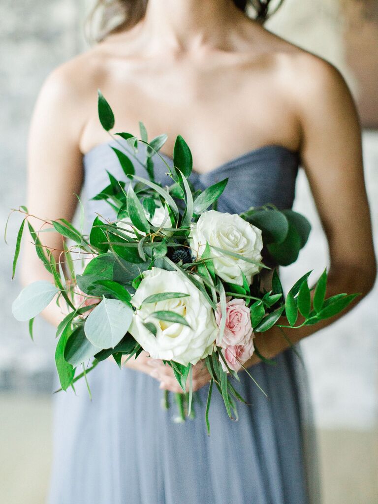 A bridesmaid holds a bouquet of roses and vibrant greenery.