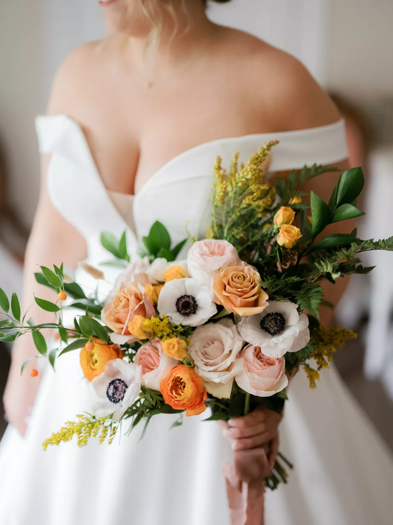 A bride holds this gorgeous autumnal bouquet with panda anemones and pink and orange roses.