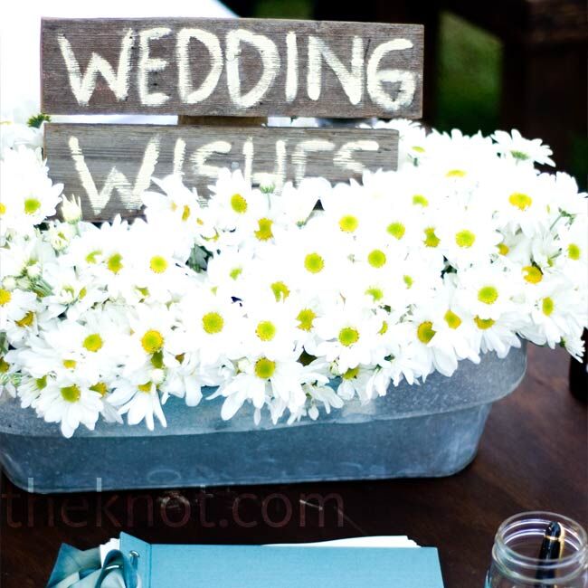Matching the centerpieces, an arrangement of white daisies in galvanized buckets decorated the guest book table. A wooded sign painted with “wedding wishes” let guests know what to do.