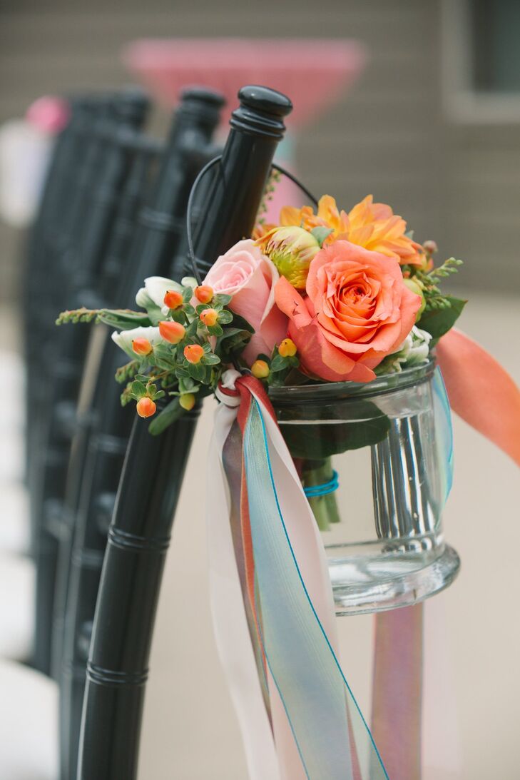 The aisles were lined with cheerful pink and coral roses accented by hypericum berries. Each festive bunch was arranged in a small glass vase decorated with colorful cascading ribbons.