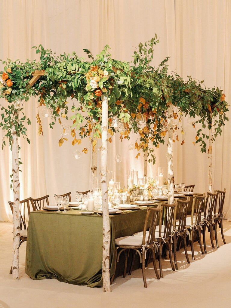 rustic wedding tablescape with birch. branch canopy and green and brown fall foliage hanging above the table