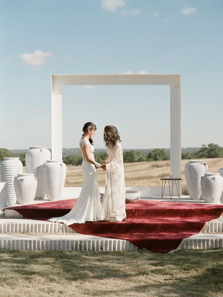 two brides standing in front of oversized white square frame overlooking hillside venue