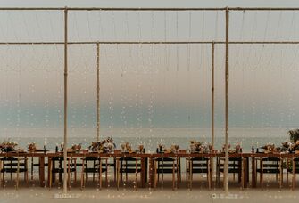 outdoor wedding venue with long banquet table surrounded by a curtain of string lights on both sides