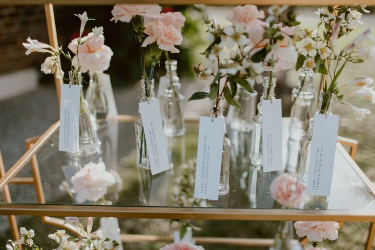 Escort cards attached to vintage bottles holding pink carnations