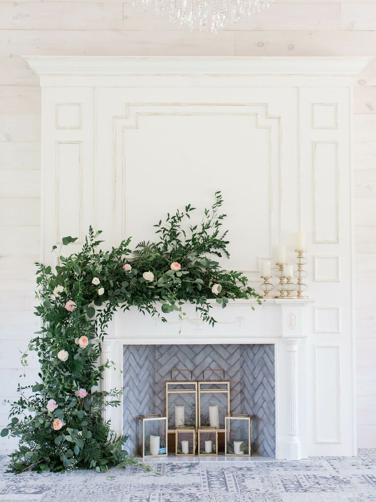 white wedding fireplace decorated with greenery, blush roses and white candles in gold square lanterns