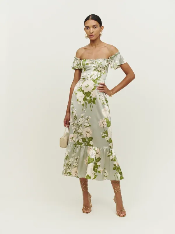 Model wears an off-the-shoulder silk dress with a pale green color scheme and floral pattern. 