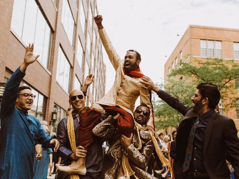 groom riding on friends' shoulders during baraat at Hindu wedding ceremony
