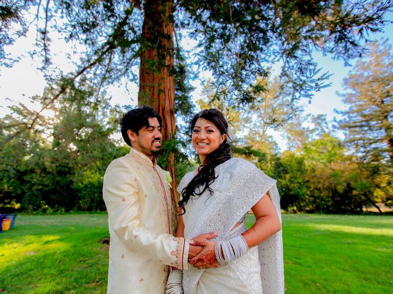 Bride wearing a white wedding sari while posing with groom.