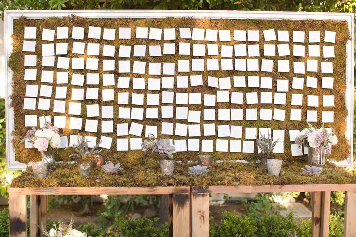 Before heading indoors for dinner and dancing, guests paid a visit to the couple’s whimsical moss-covered seating chart to find the escort cards that would lead them to their tables. The cards were pinned to a backdrop of moss displayed in an antiqued white frame, which was surrounded by potted succulents and white and purple blooms.