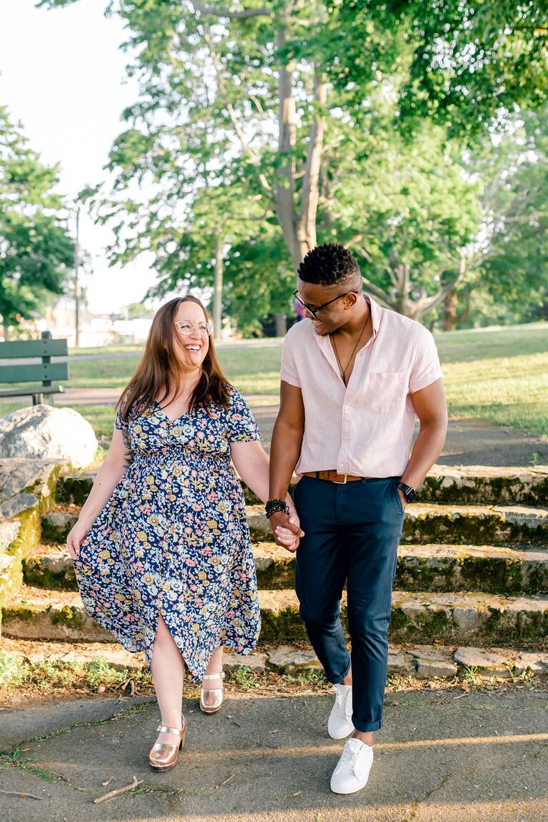 Couple walks hand-in-hand through park during sunset engagement photo shoot
