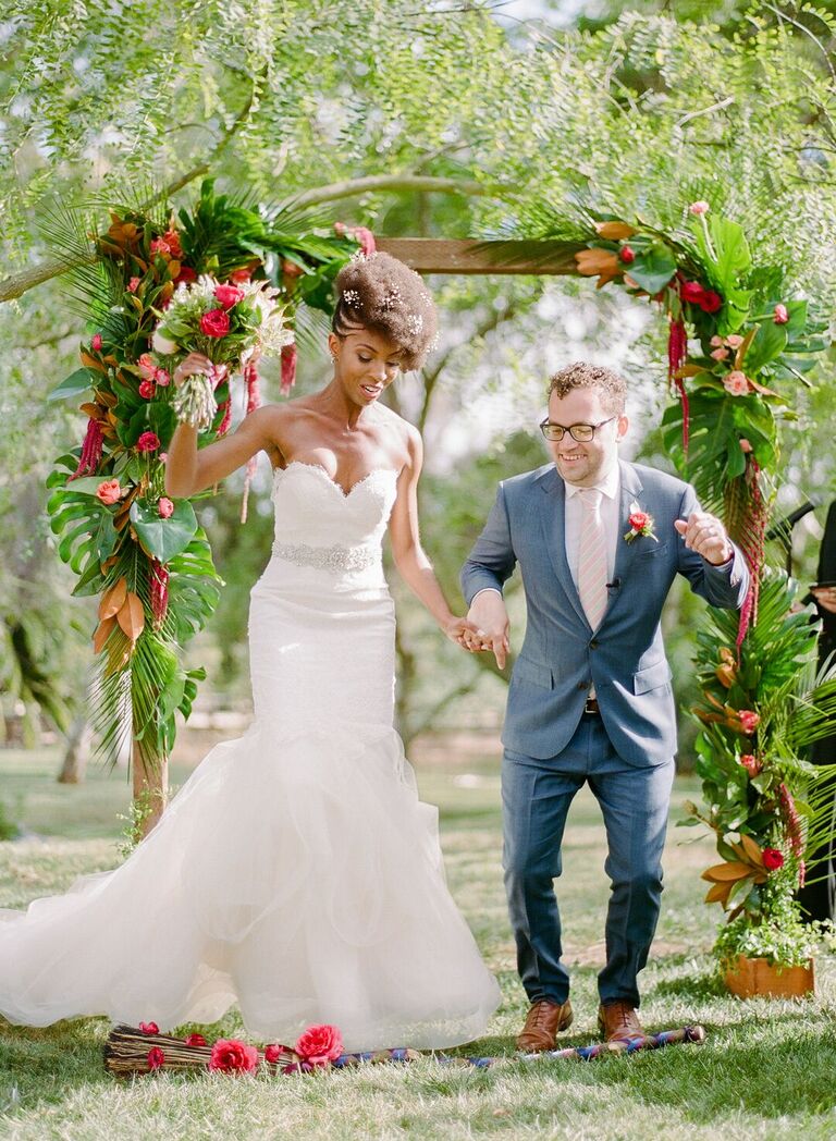 Couple jumping the broom at tropical wedding ceremony