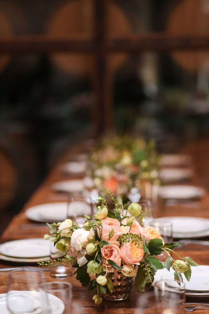 Emma and Jesse looked to bunches of textured, peach, ivory and coral flowers to bring their rustic reception tables to life. Mercury glass vases ran the length of the table, bearing cascades of roses, wildflowers, peonies, vines and leaves. To create a sense of cohesion between each of the decor elements, the pair dressed the tables with vintage floral dinnerware.