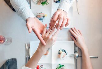 Restaurant proposal with groom putting engagement ring on his partner