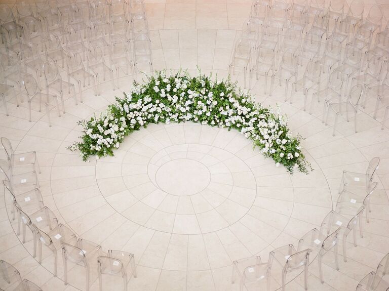aerial view of indoor wedding ceremony with ghost chairs arranged in a circular shape and floral arch at the center