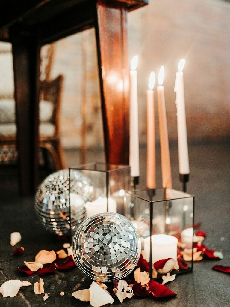 Tapered neutral candles next to disco balls and flower petals and bohemian wedding