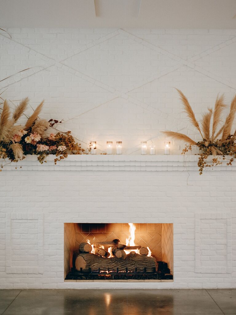boho wedding fireplace decoration idea with pampas grass, dried flowers and votive candles against white brick mantel