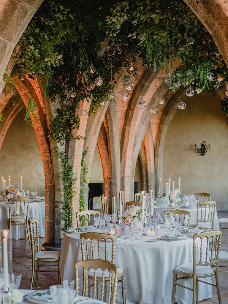Architectural wedding reception space with while tables and suspended greenery