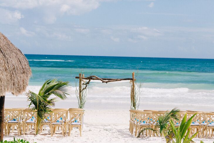 Danielle and Jason had a traditional Jewish ceremony on the beach underneath a driftwood chuppah at Akiin Beach Club in Tulum, Mexico. Light wooden furniture with turquoise accents and greenery created a rustic, natural atmosphere.