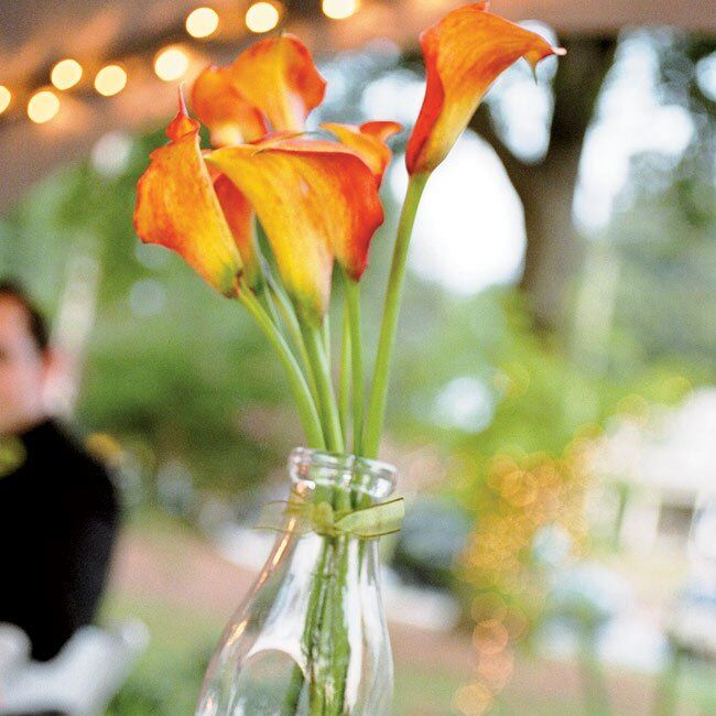 Diane bought dark metal pillar candle holders and candles in various sizes, which she grouped and placed on half of the tables. For the other tables Diane and her mother used old milk bottles from Diane’s grandfather’s dairy farm, and filled them with black river stones and glass beads with mango calla lilies. To bring in the green, Diane’s grandmother made green fabric squares for underneath each centerpiece.
