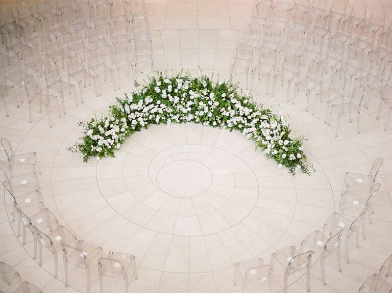 aerial view of wedding ceremony with clear acrylic ghost chairs set up in a circle and greenery arch with white flowers at the center
