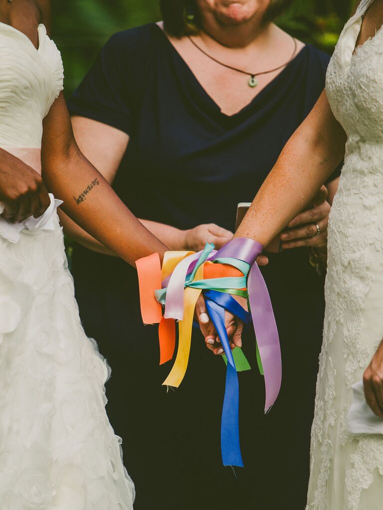 Brides holding hands during colorful ribbon binding unity ceremony