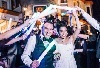 Bride and groom surrounded by their guests holding glow sticks.