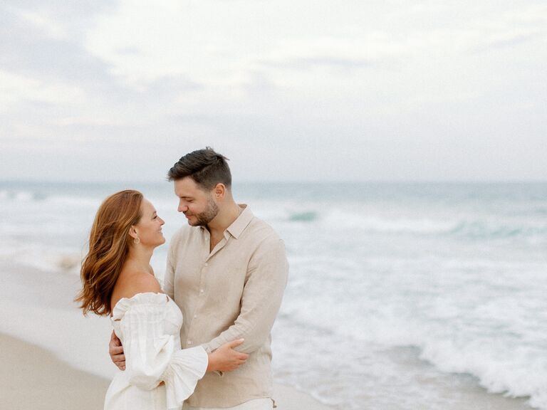 Couple embrace and look at each other lovingly on a beach. 