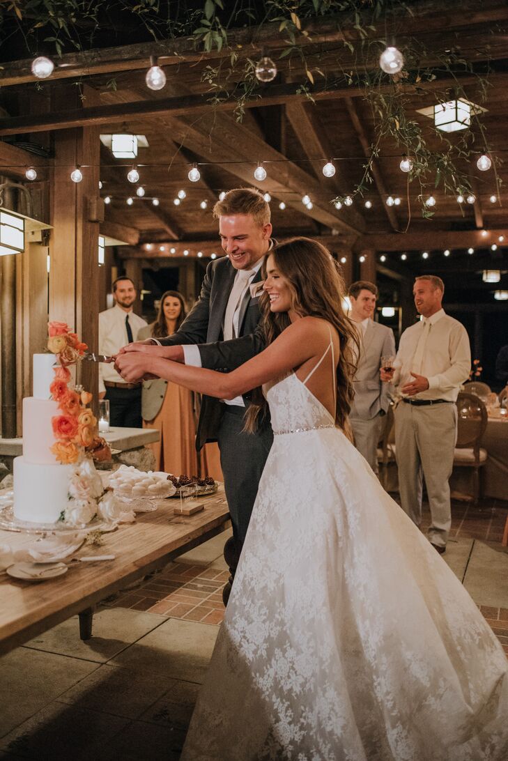 Bride and Groom Cutting Into Wedding Cake Under String Lights