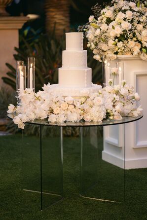 Glass Cake Table, White Flowers, Candles and Tiered White Wedding Cake With Intricate Designs