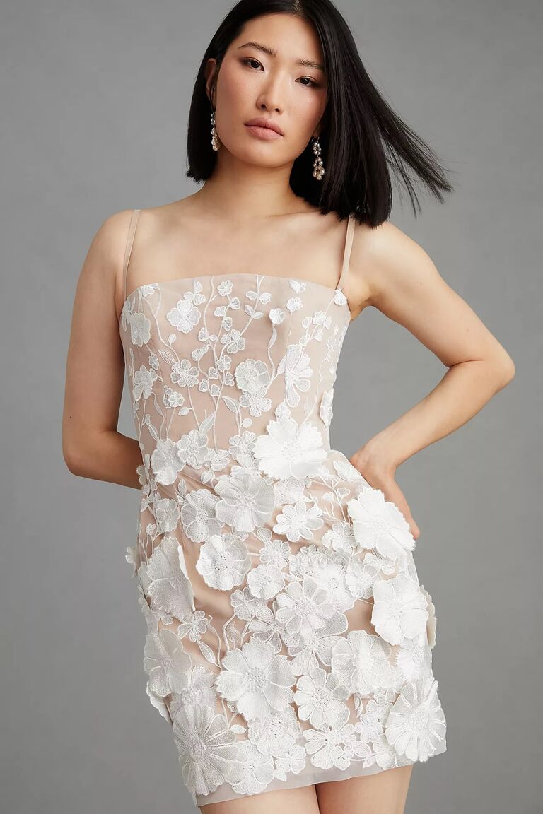 Model wears a short structured mini dress with floral detailing. 