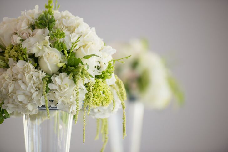 Dramatic floral arrangements in tall glass trumpet vases framed the ceremony. They consisted of white roses, hydrangeas, lisianthus, freesia, mini green hydrangeas, Bells of Ireland and hanging amaranthus.