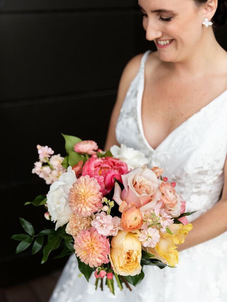 Bride holds a beautiful bouquet of pink dahlias and roses. 