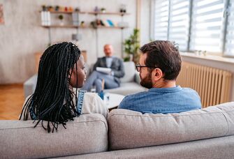 couple sitting side by side on a couch with a therapist opposite them