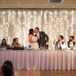 Behind the head table, a curtain of sheer fabric and fairy lights illuminated the space.